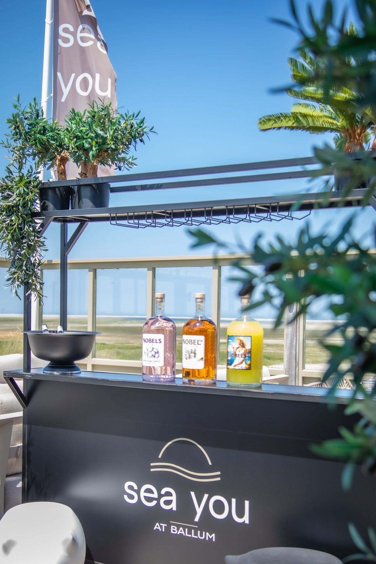Het interieur van Sea You at Ballum met olijfboom, rieten lampen en het Sea You neon bord